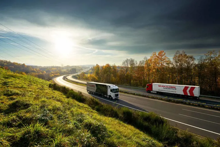 Two Scan Global Logistics trucks driving on a scenic highway at sunrise, symbolizing efficient track and trace technology